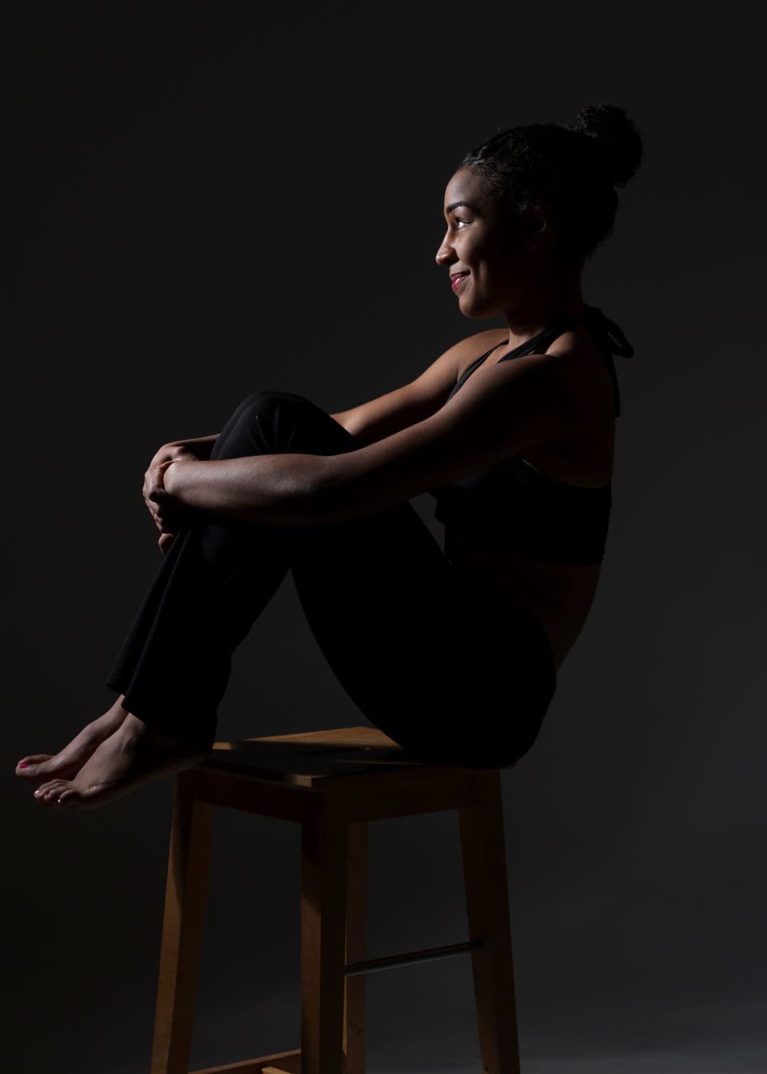 Femme assise sur un tabouret en tenue de sport, profil dans une lumière douce sur fond sombre