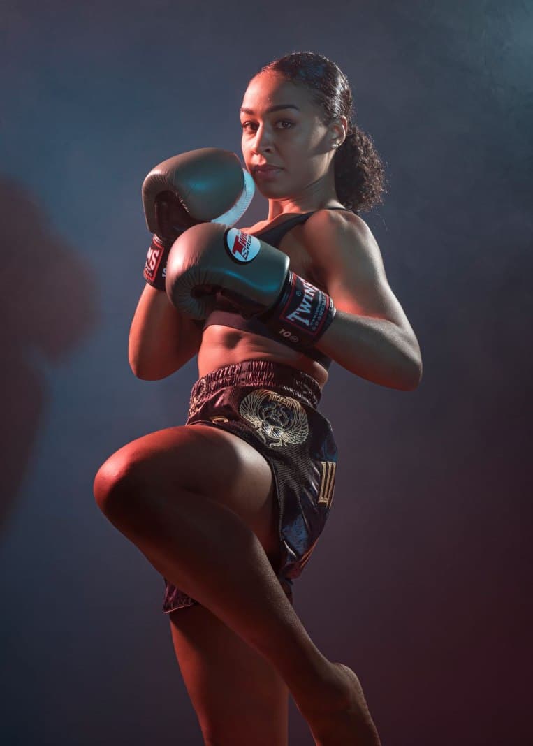 Sportive en gants de boxe levant un genou en garde de kick-boxing, éclairage coloré en studio