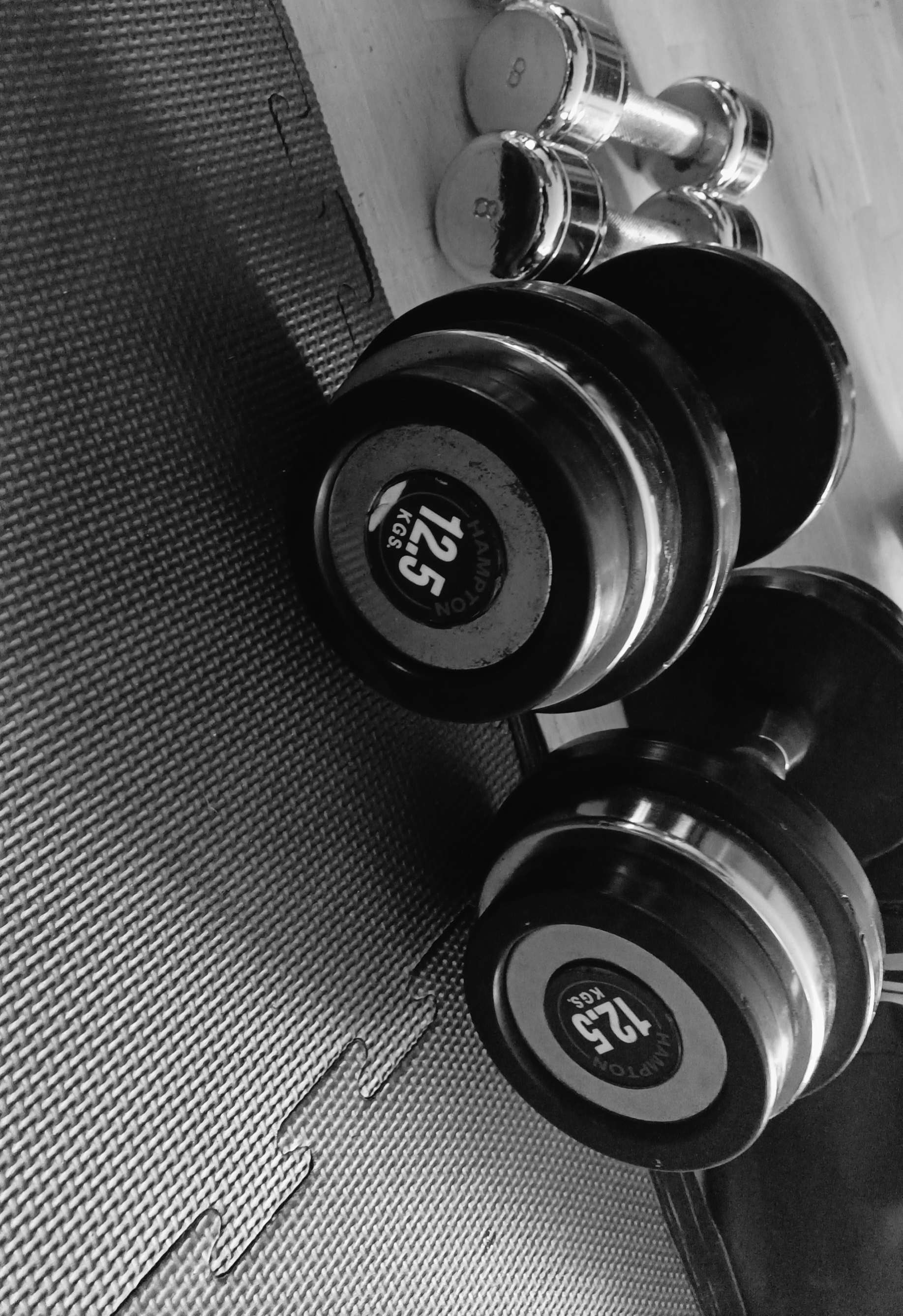 Haltères et poids de musculation sur un tapis de gym, en noir et blanc.