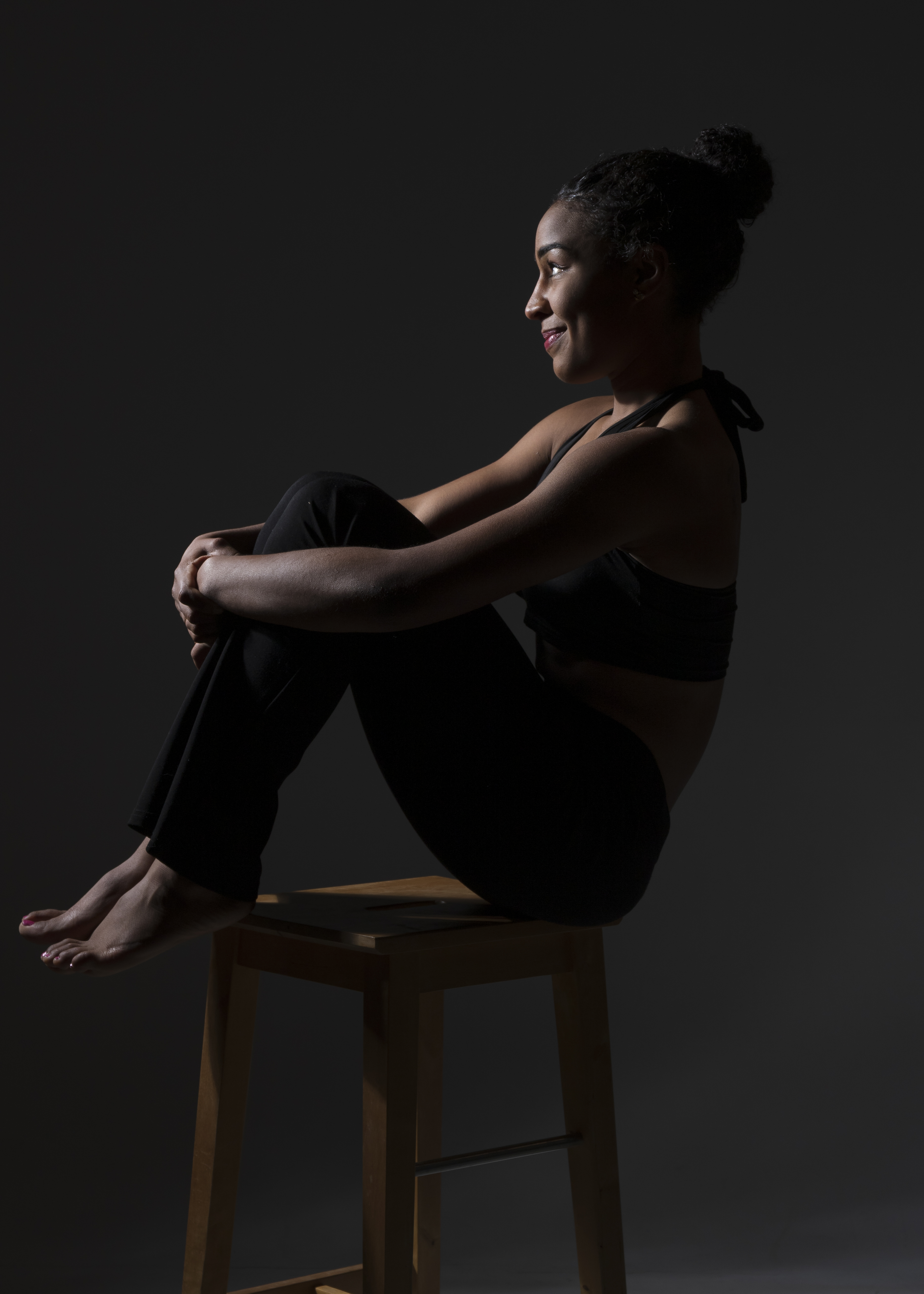 Femme en tenue de sport assise sur un tabouret, en posture de relaxation, éclairage tamisé.