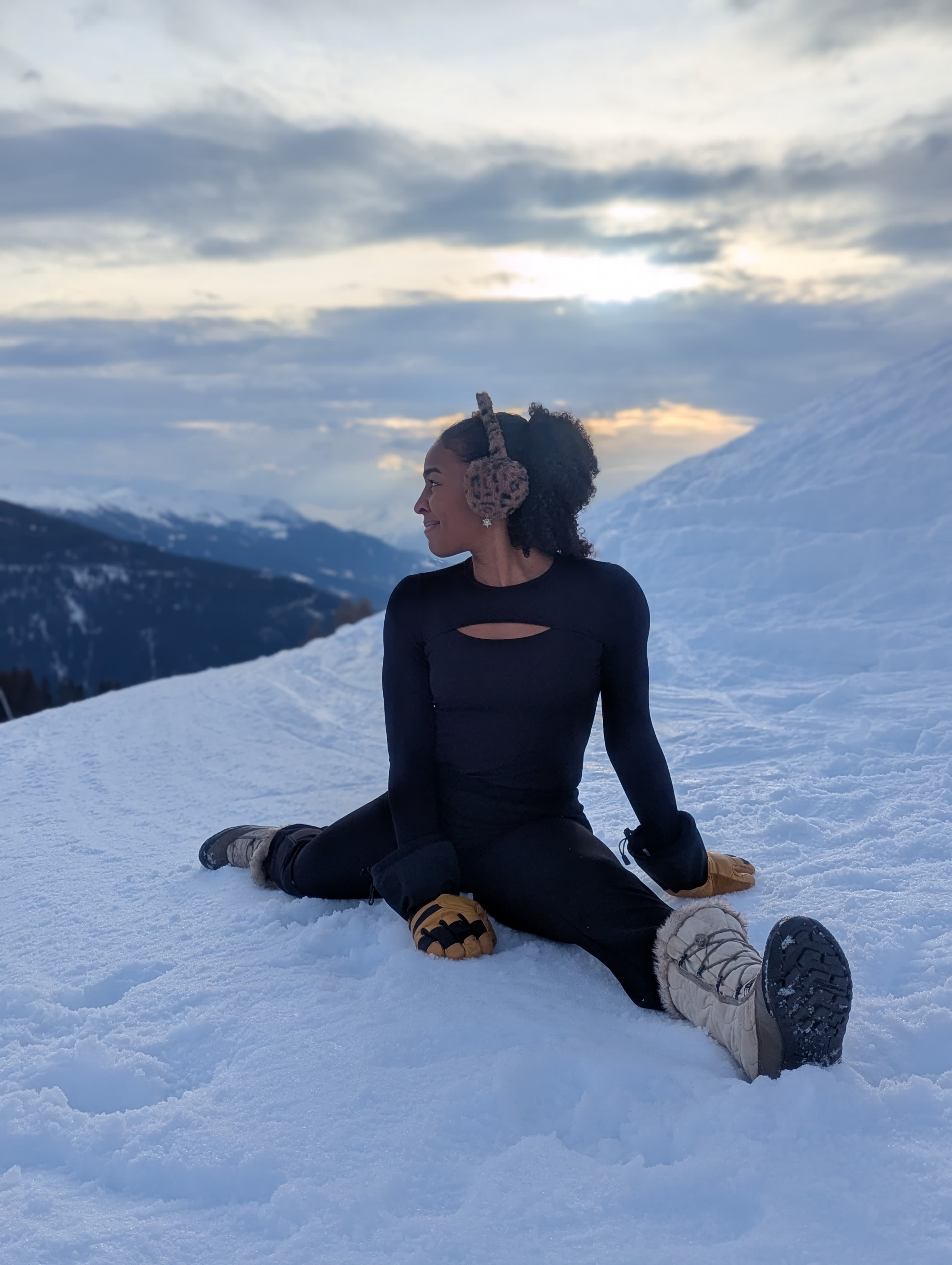 Personne effectuant un étirement et du stretching dans la neige, avec une vue sur des montagnes enneigées.